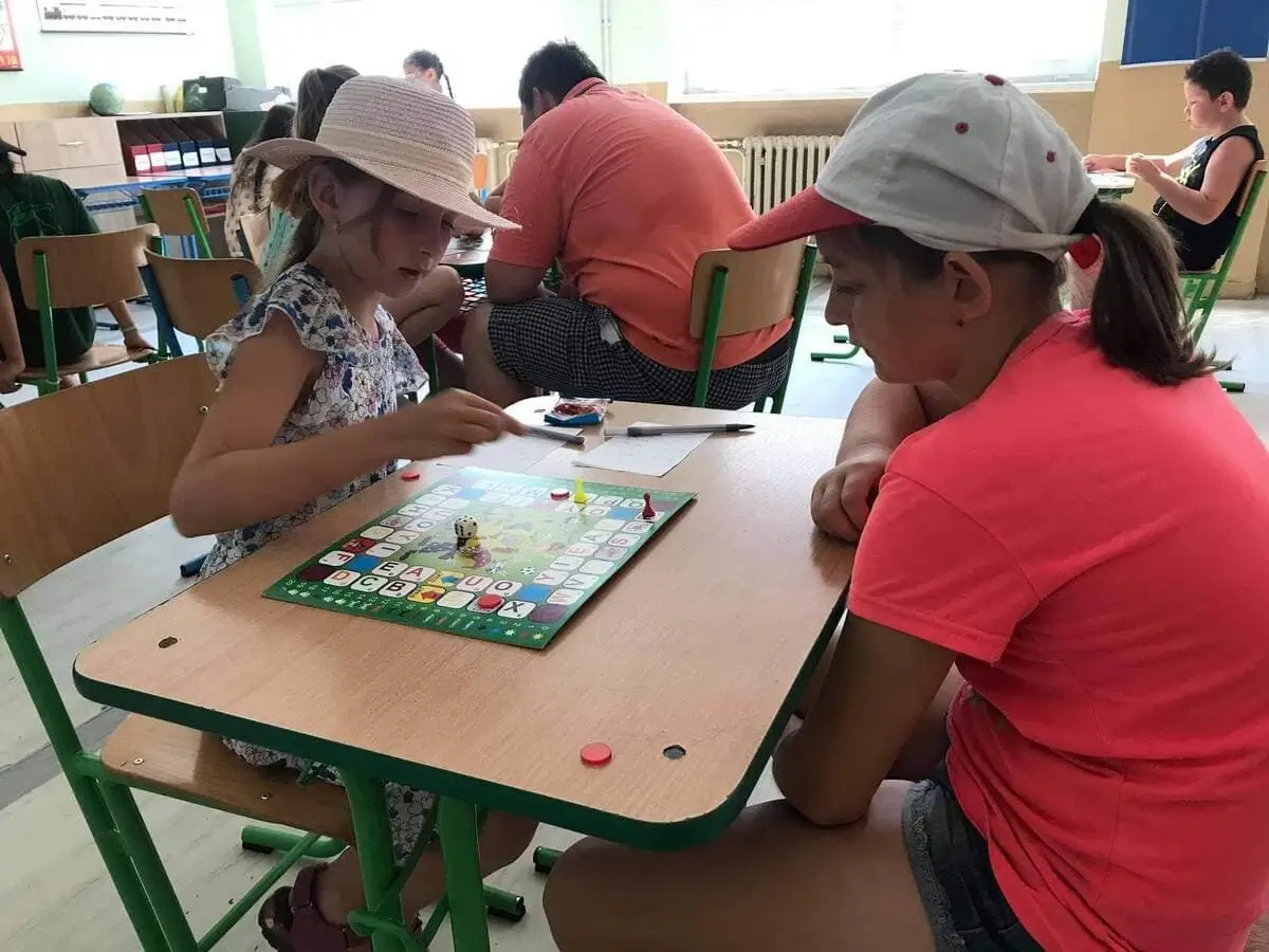 Dve dievčatá sústredene hrajú edukačnú hru Magické písmenká v školskej triede počas letnej aktivity