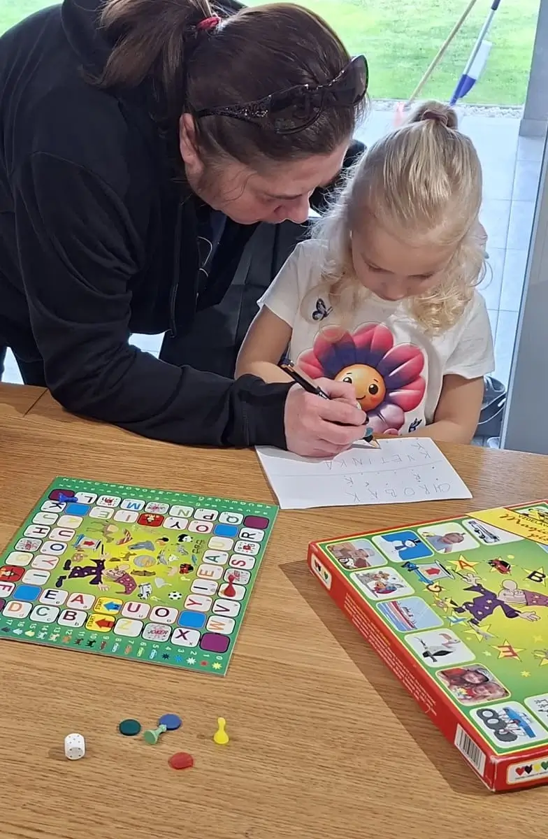 Babka ukazuje dievčatku ako napísať jej meno pri edukačnej hre Magické písmenká s otvorenou krabicou
