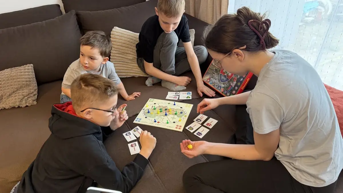 Rodinná partia hra Slovensko od Miaplay s kartičkami miest a štyrmi deťmi zahĺbenými do stratégie